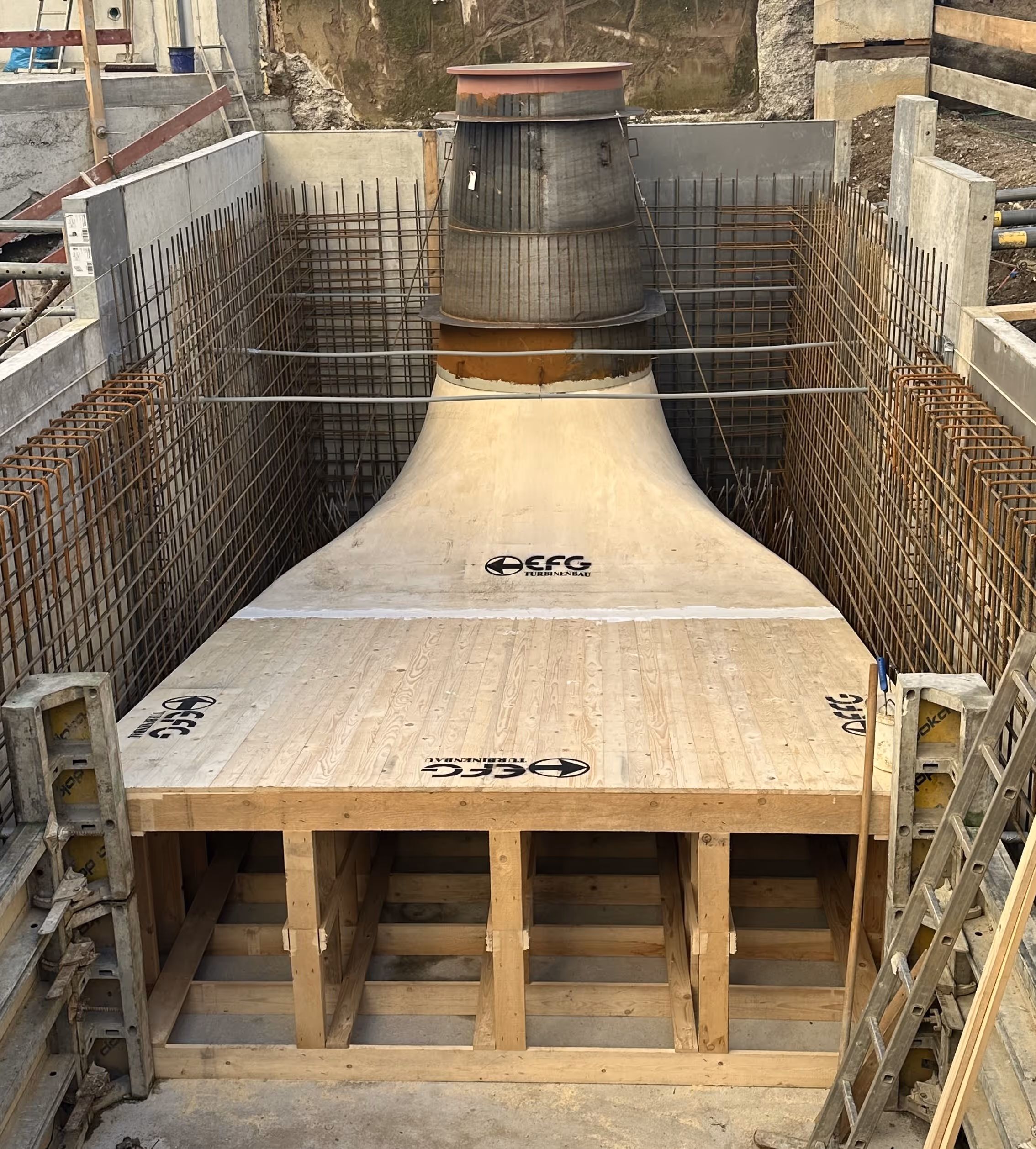 Construction site showing a large turbine component surrounded by steel rebar and wooden framework.