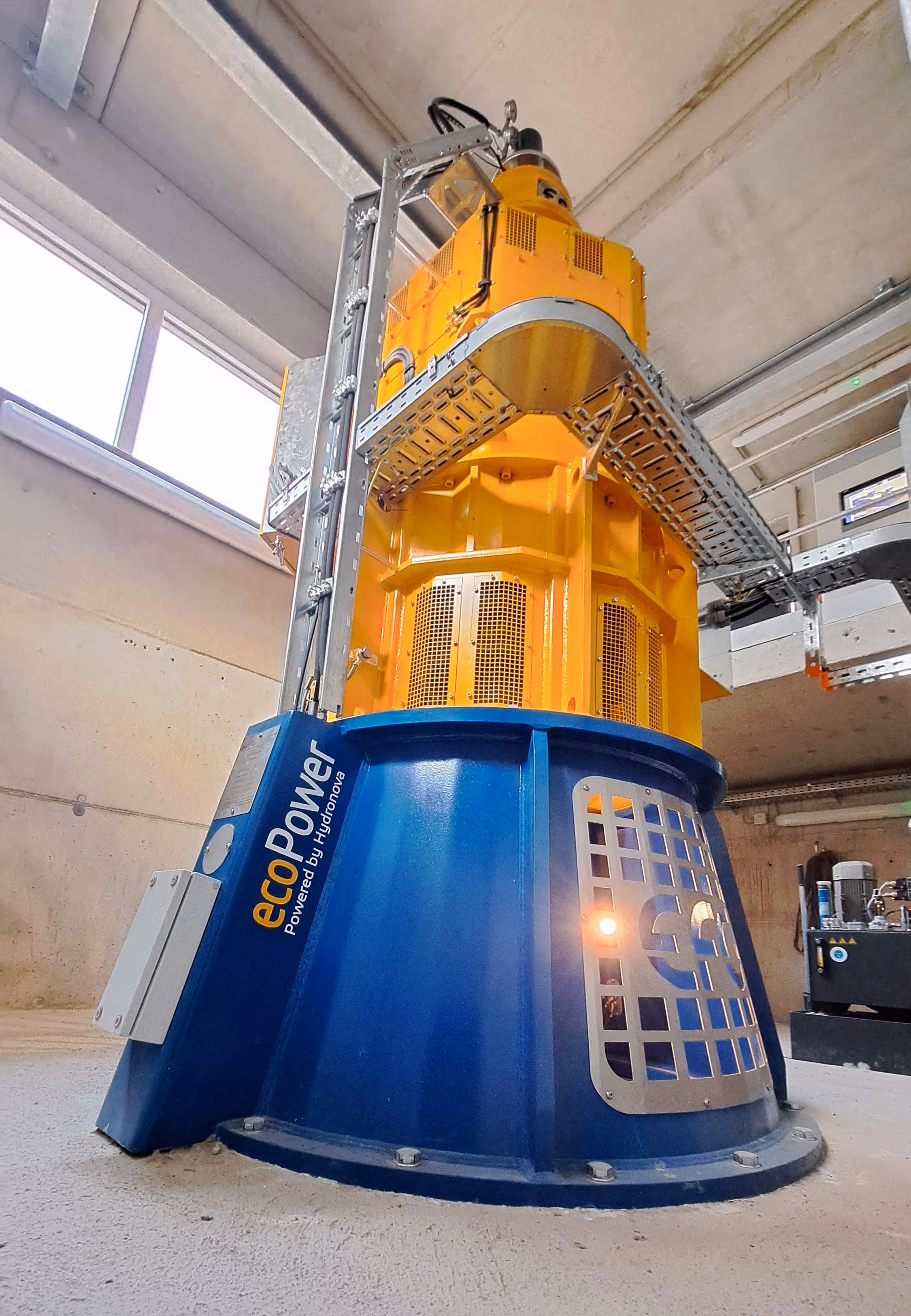 Tall industrial ecoPower machine in blue and yellow inside a concrete facility with metal fixtures.
