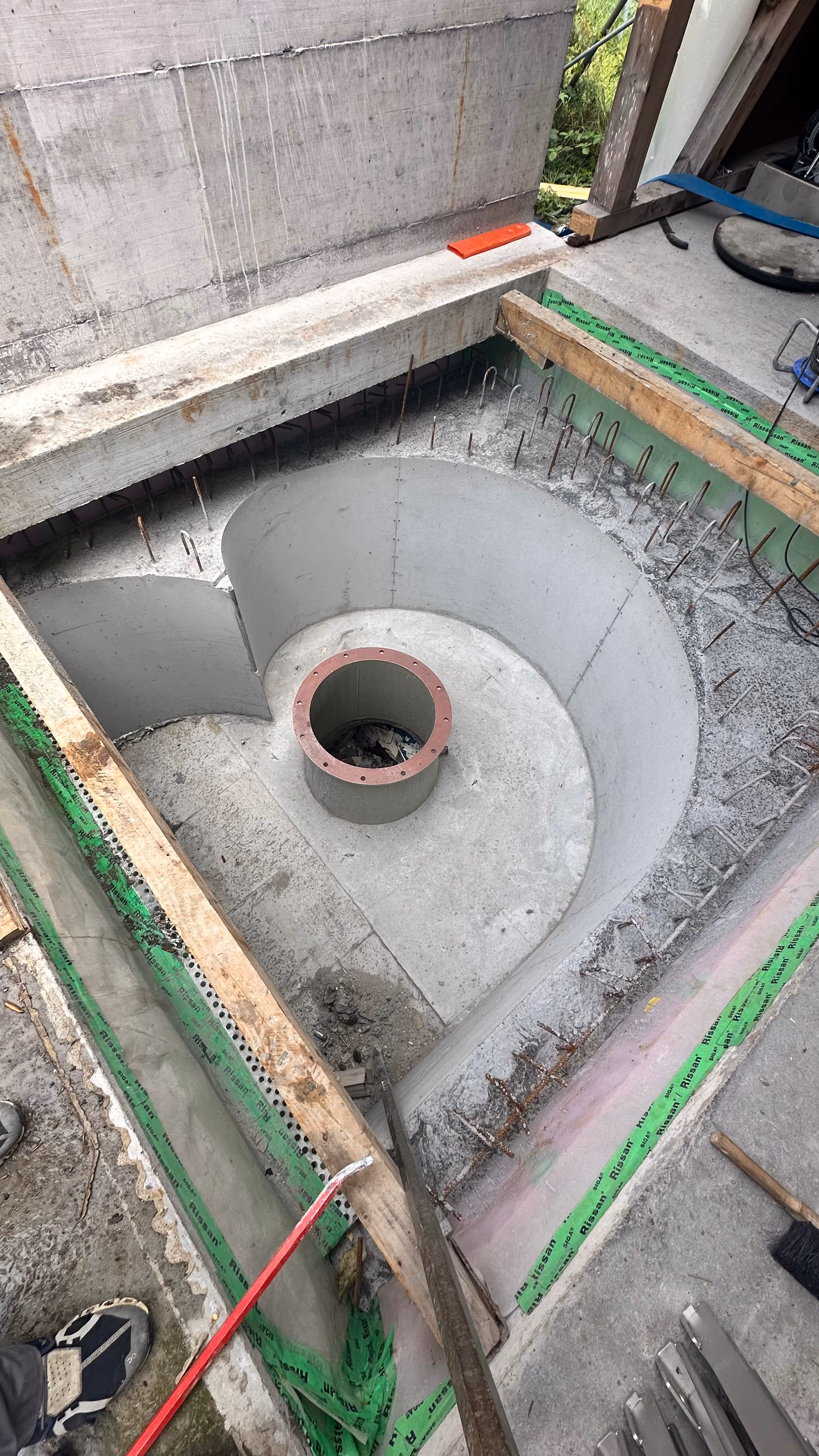 Construction site with a concrete circular structure reinforced with metal rods and wooden framing surrounding it.