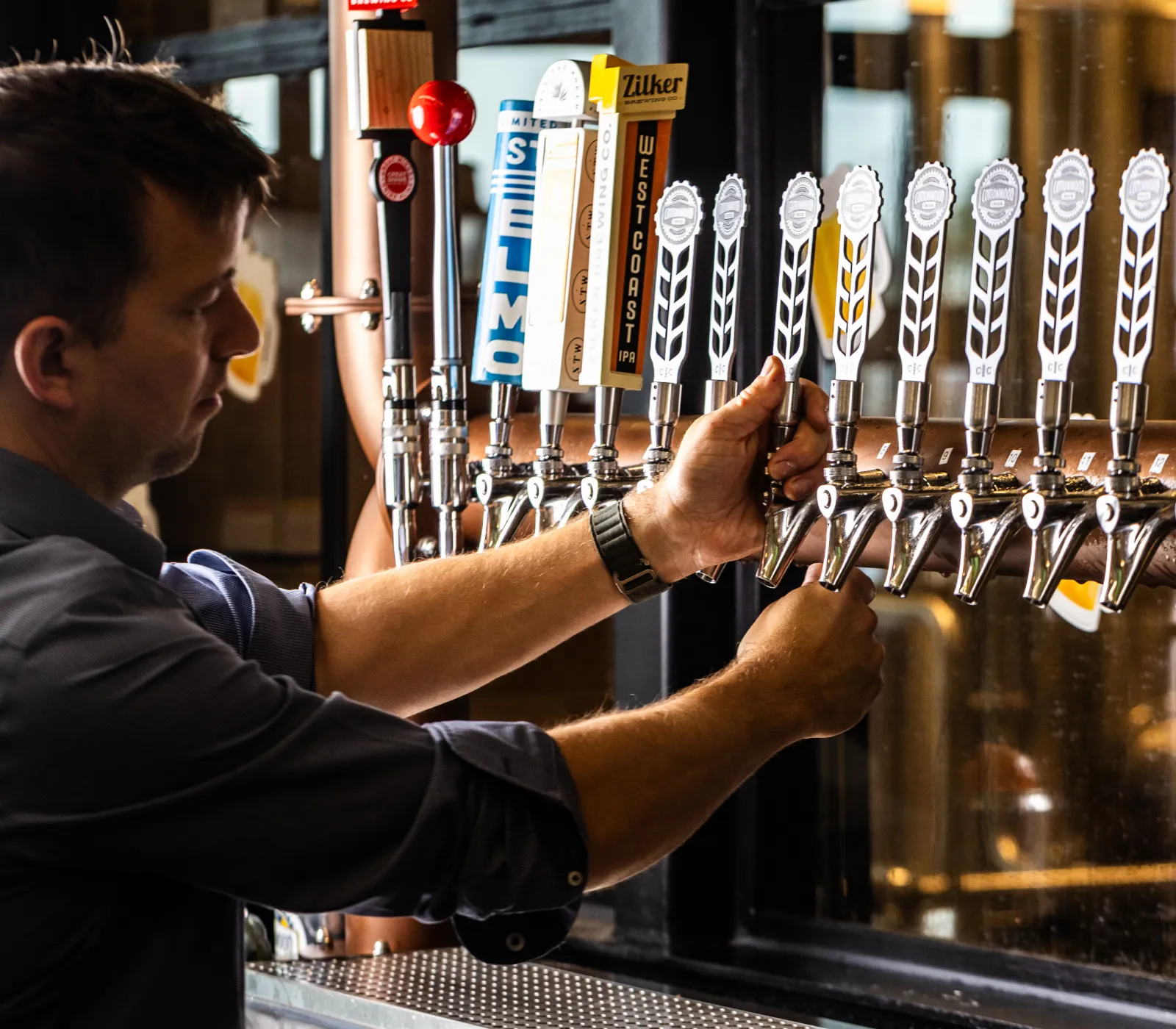 Man pouring draft beer from taps in a bar with multiple branded tap handles.