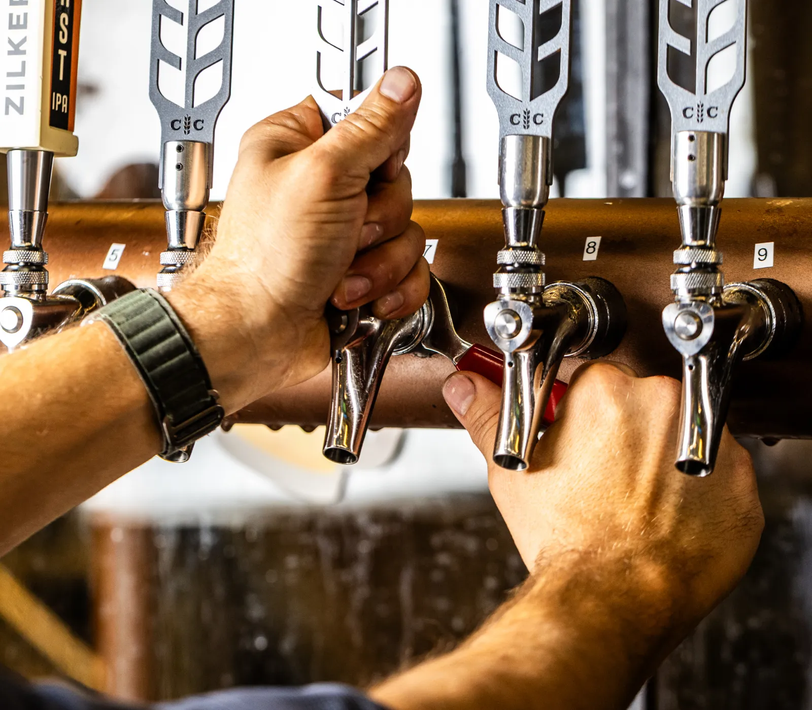 Hands pulling beer tap handles numbered 7 and 8 in a bar or brewery.