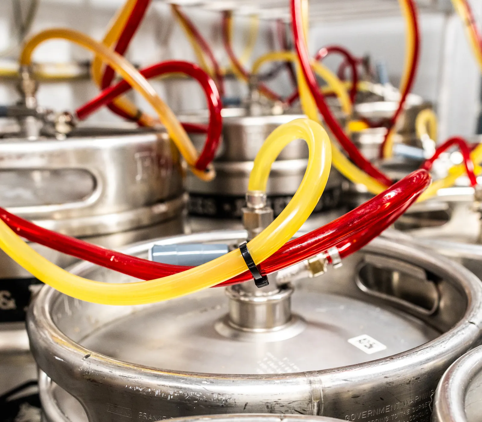 Rows of metal kegs connected to a complex system of gauges and red and yellow tubes in a beverage dispensing setup.