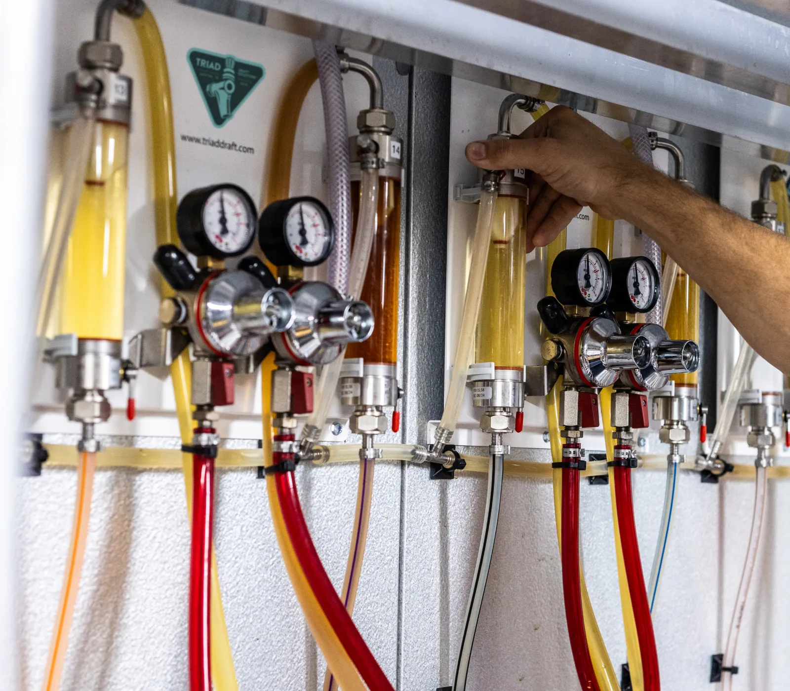 Hand adjusting valves on a wall-mounted array of brewing or beverage gas regulators and flow meters with connected tubes.