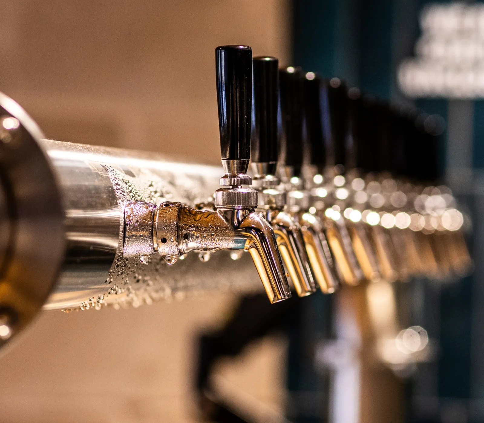 Close-up of a row of brewery or bar beer taps with black handles and condensation on the metal surface.