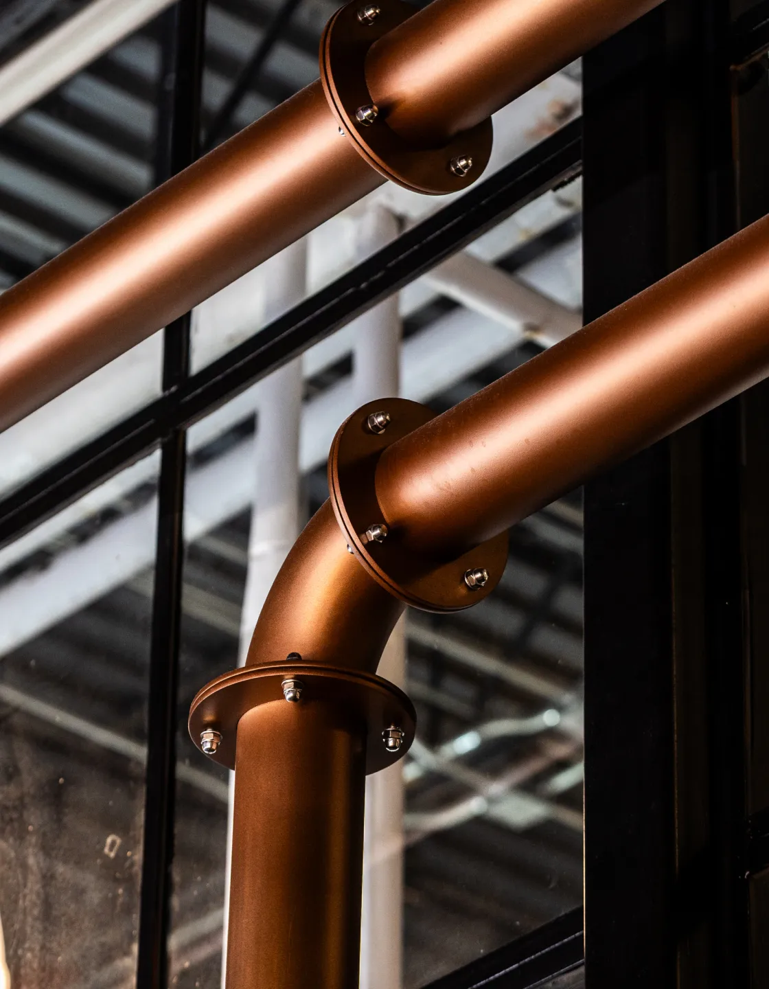 Close-up of industrial copper-colored metal pipes with flanged joints inside a building.