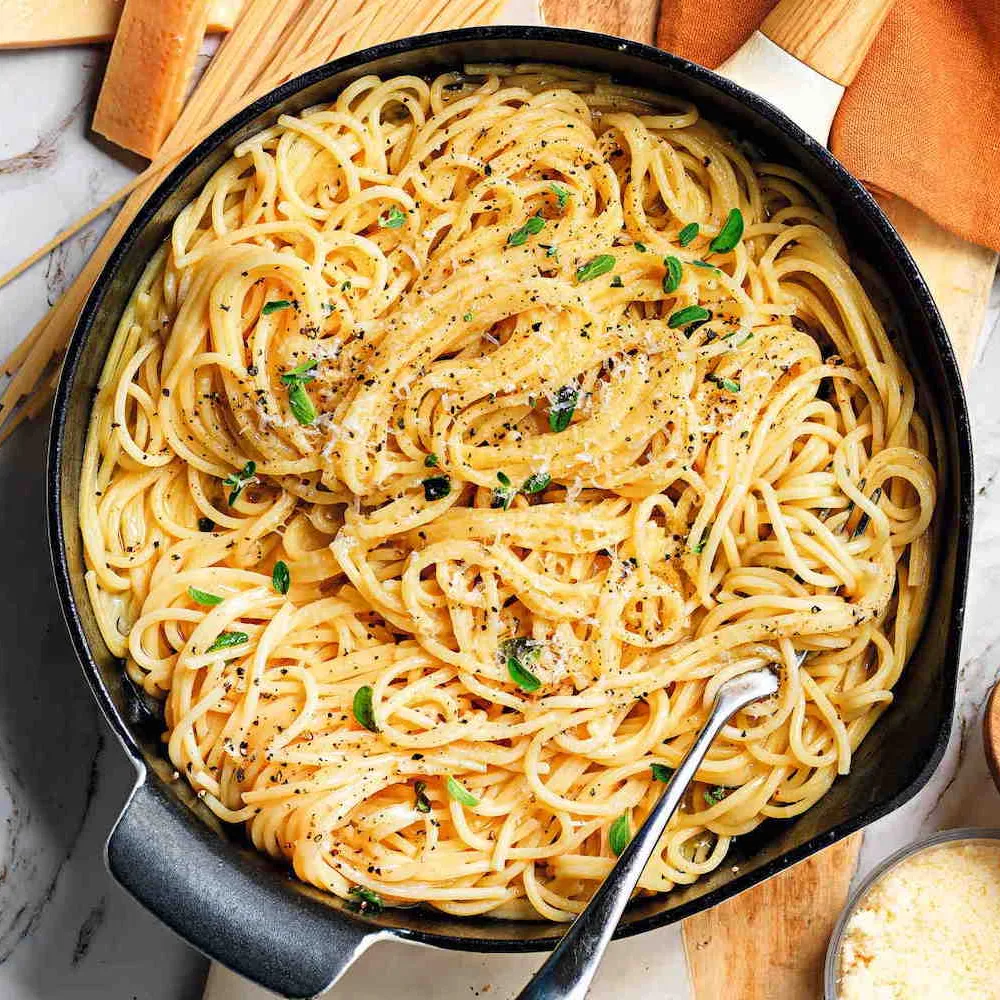 Padella di pasta spaghetti condita con formaggio, pepe e foglie di erbe fresche.