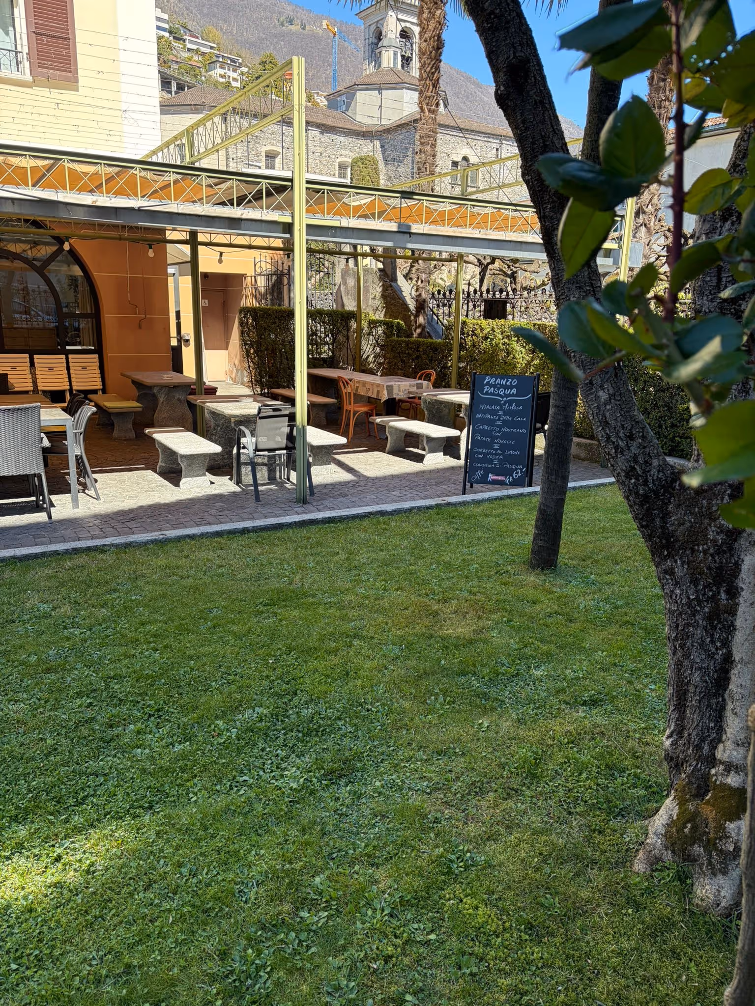 Spazio esterno di un ristorante con tavoli, panche e una lavagna con il menu del pranzo di Pasqua.