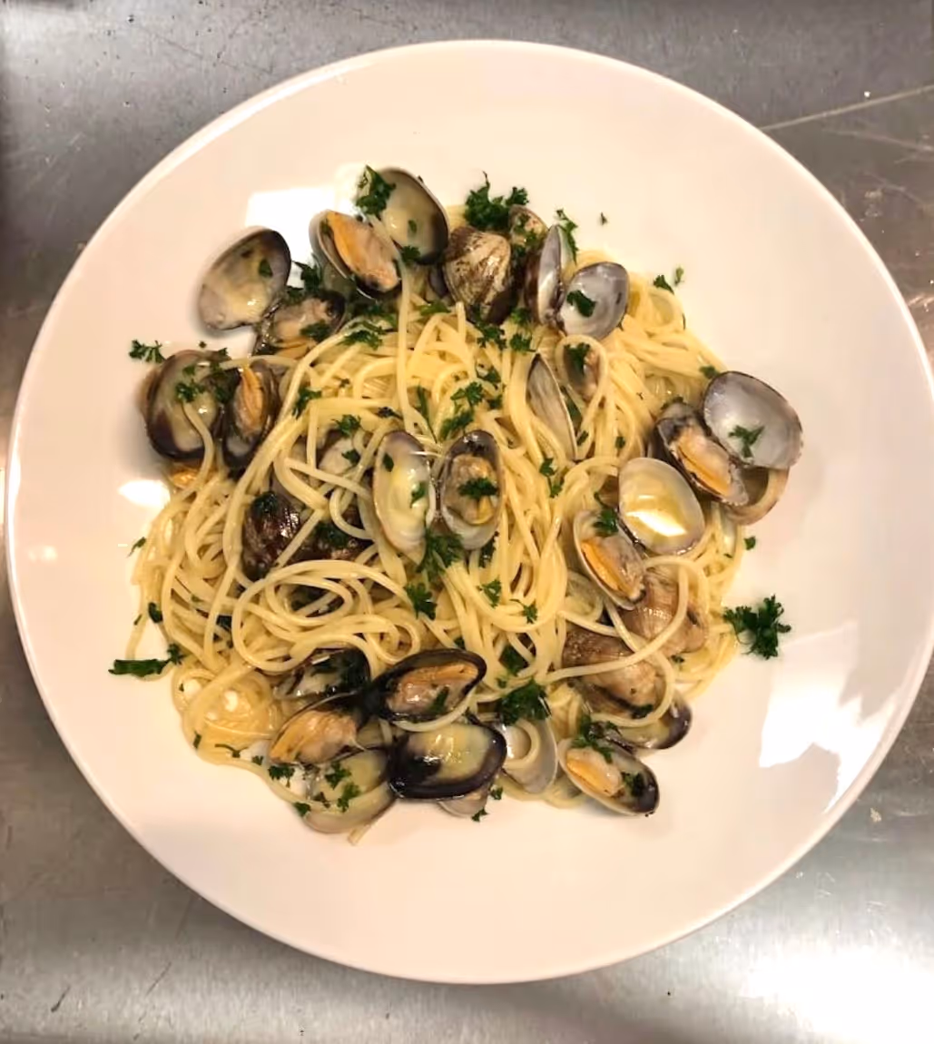 Piatto di spaghetti con vongole e prezzemolo su un tavolo metallico.
