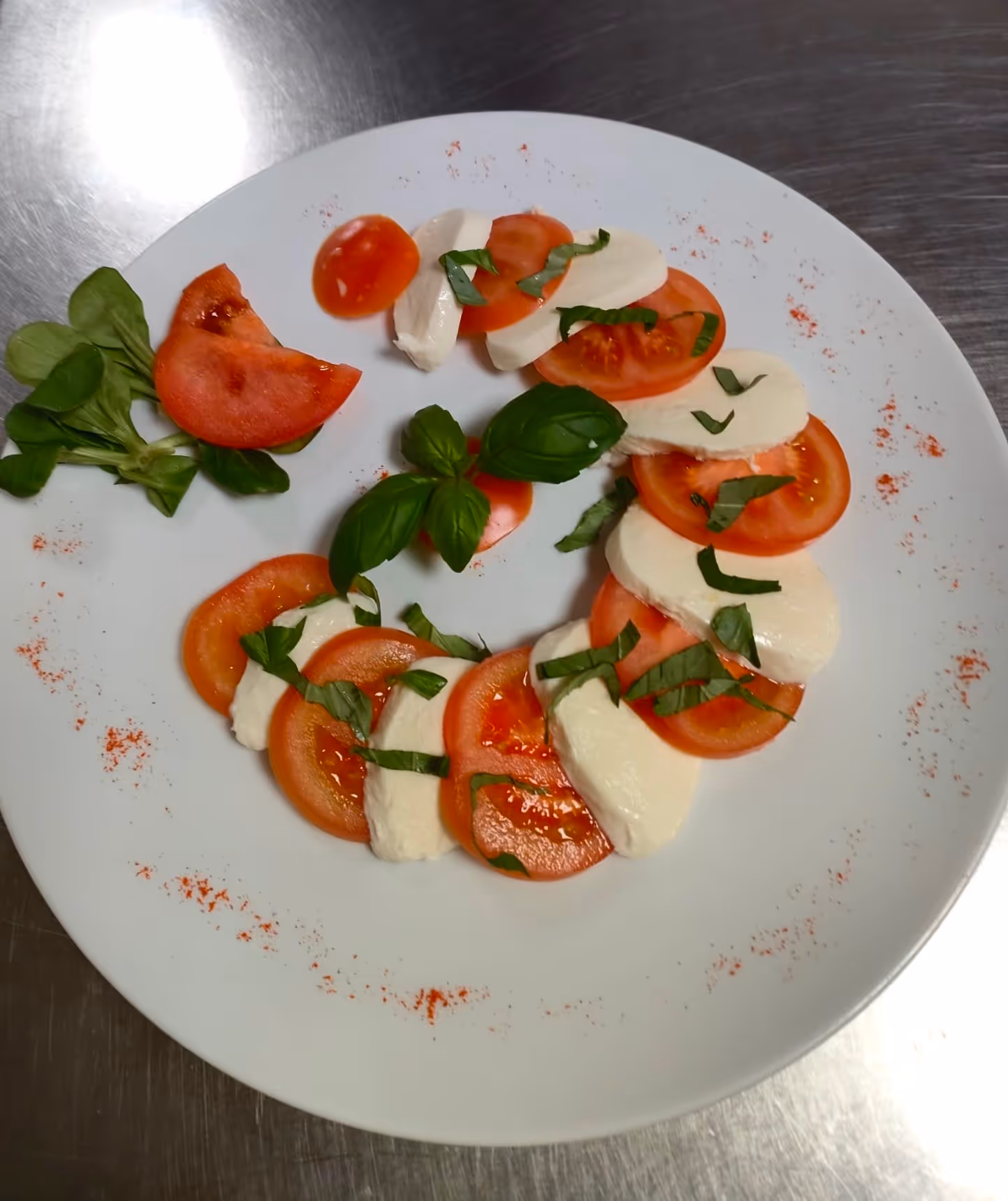 Insalata caprese con fette di pomodoro, mozzarella e basilico su un piatto bianco.