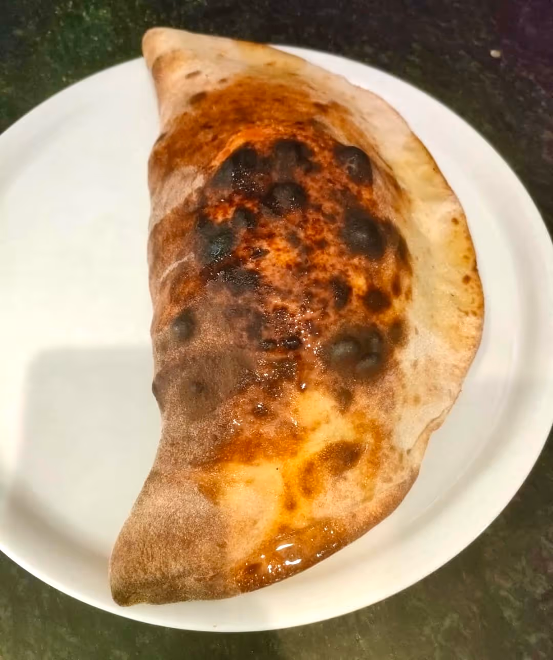 Calzone con crosta dorata e brunita su un piatto bianco.