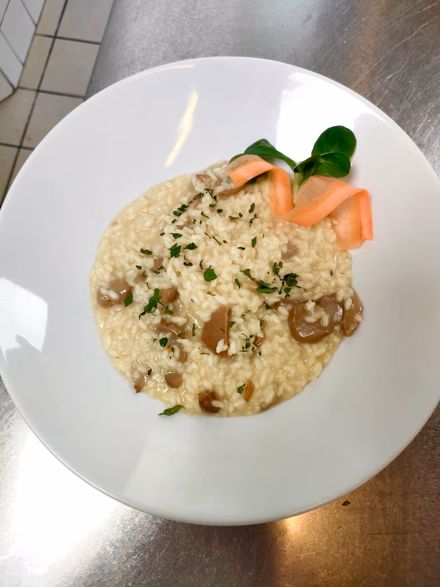 Risotto cremoso con funghi, guarnito con prezzemolo, una foglia verde e una fettina di carota.