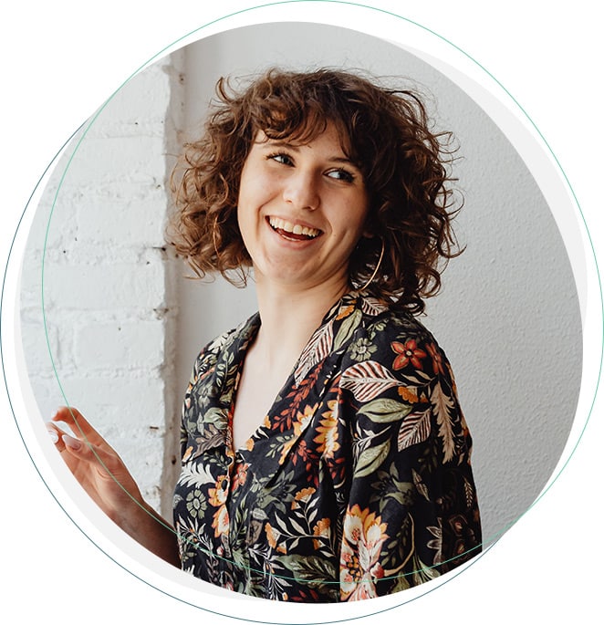 Smiling woman with curly hair wearing a floral patterned blouse against a white wall.