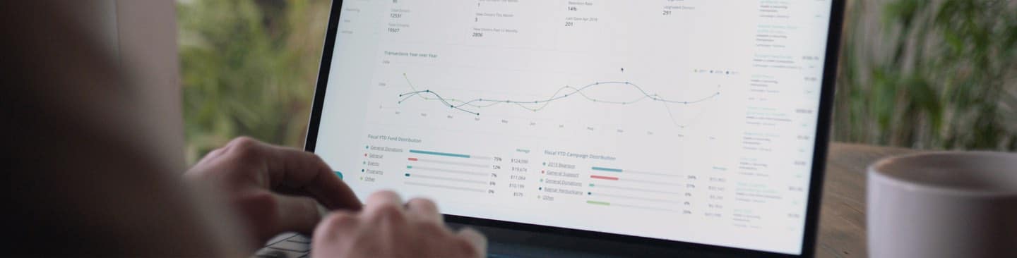Person typing on a laptop displaying financial charts and data visualizations on screen.