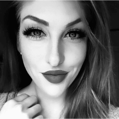 Black and white close-up of a smiling woman with long hair, wearing makeup and holding her collar.