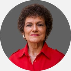 Portrait of a mature woman with short curly hair wearing a red shirt and pearl earrings.