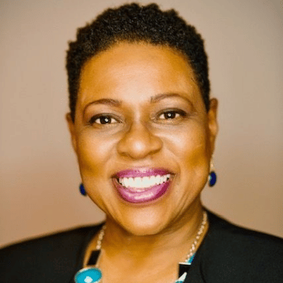 Smiling woman with short hair wearing blue earrings and necklace with turquoise pendant.