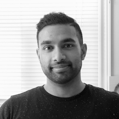 Headshot of a man with short hair and a trimmed beard wearing a dark speckled shirt in front of blinds.