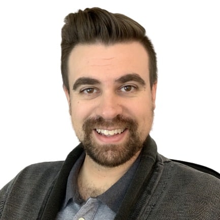 Smiling man with short brown hair and beard wearing a gray jacket and blue shirt on white background.