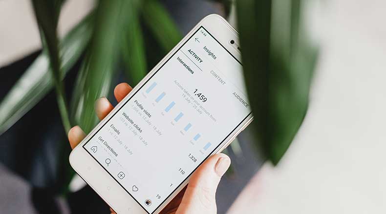 Hand holding smartphone showing social media insights with activity stats and interactions chart.
