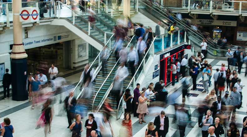 Busy London underground station with blurred commuters using escalators and walking in the concourse.