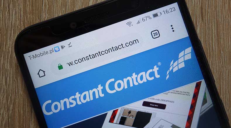 Smartphone displaying the Constant Contact website header on a wooden surface background.