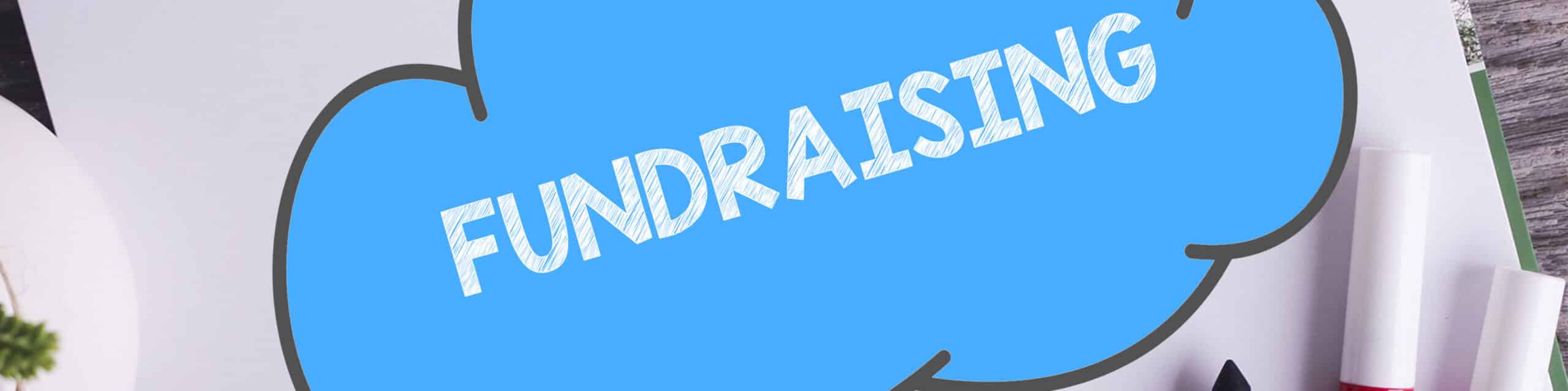 Blue speech bubble with the word FUNDRAISING on a desk with office supplies and plants.