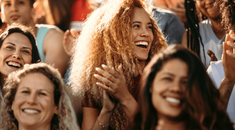 Group of diverse people smiling and clapping at an outdoor event in warm sunlight.