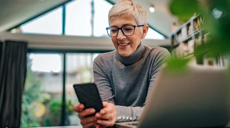 Smiling woman with short blond hair and glasses looking at her smartphone indoors.