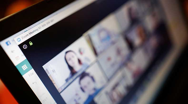 Close-up of a tablet screen showing a blurred Zoom video call with multiple participants.