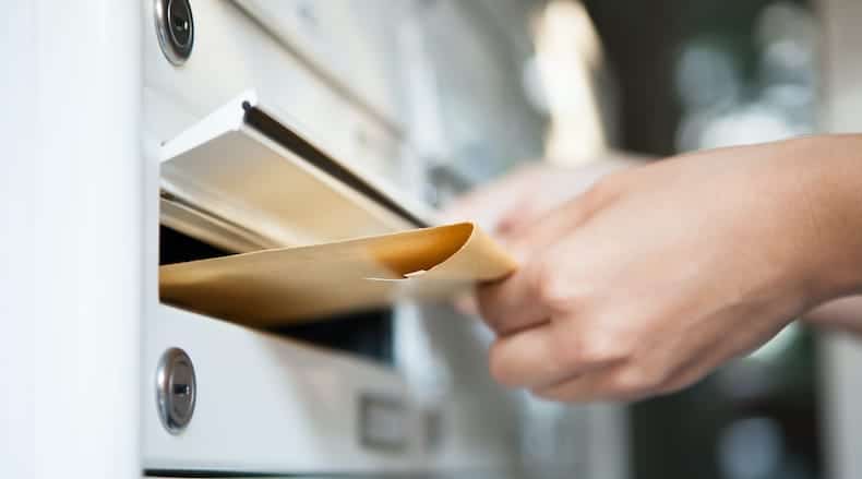 A person placing a brown envelope into a white mailbox slot.
