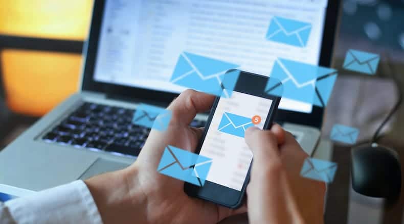 Hands holding smartphone with new email notifications against laptop and floating email icons.