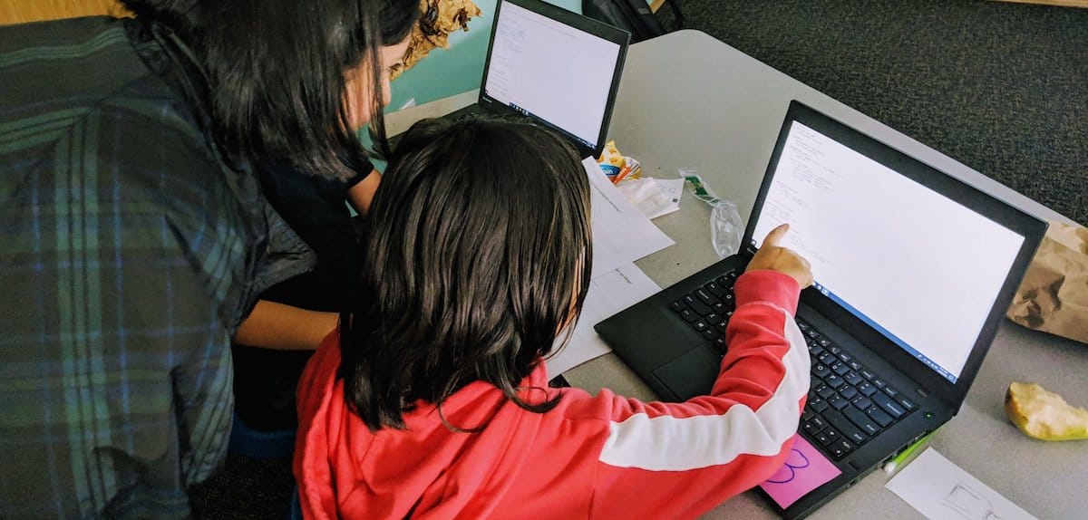 Teacher guiding child in writing computer code on a laptop