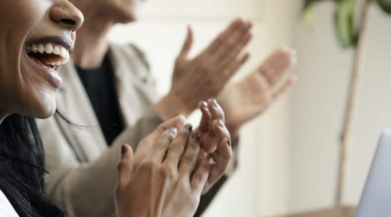Close-up of two people clapping and smiling in an indoor setting.