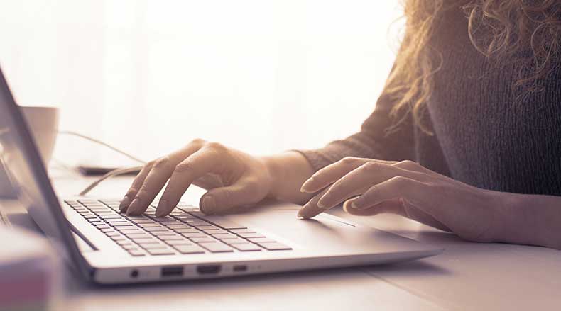 Person typing on a laptop keyboard with soft natural light coming from the background.