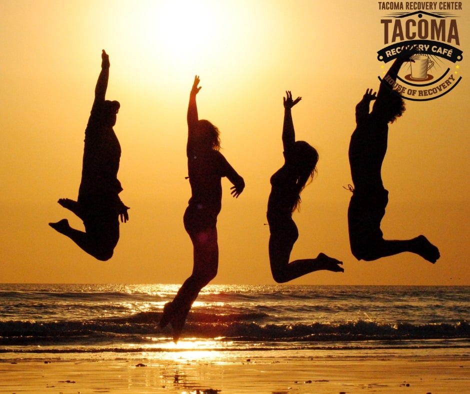 Silhouettes of four people jumping on a beach at sunset over the ocean waves.