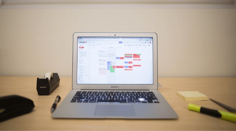MacBook Air on a desk showing a colorful digital calendar with a pen and yellow highlighter nearby.