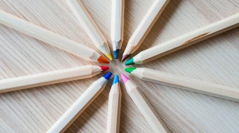 Colored pencils arranged in a circle with tips pointing inward on a wooden surface.