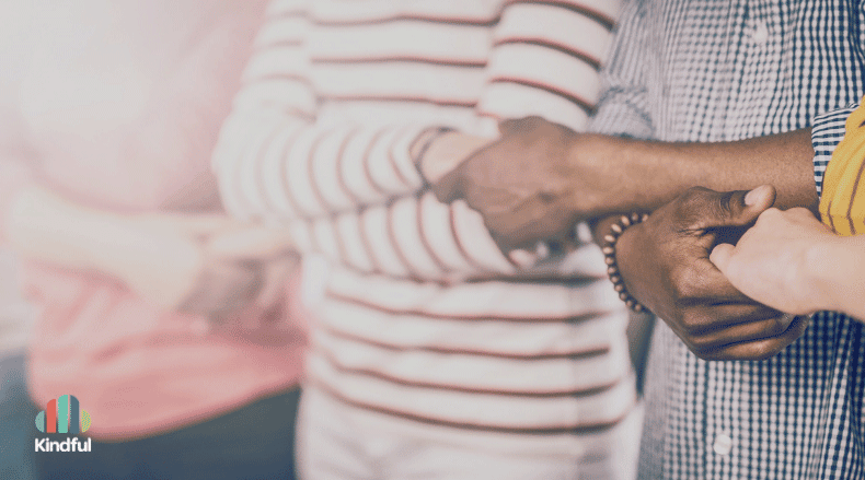 Close-up of diverse people standing in a circle holding hands in support.