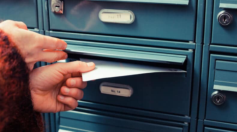 Person retrieving an envelope from a blue numbered mailbox labeled No. 14.