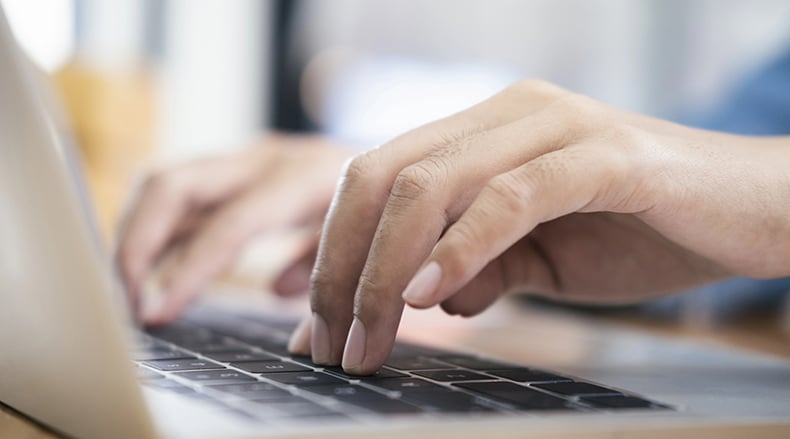 Close-up of hands typing on a laptop keyboard with a blurred background.