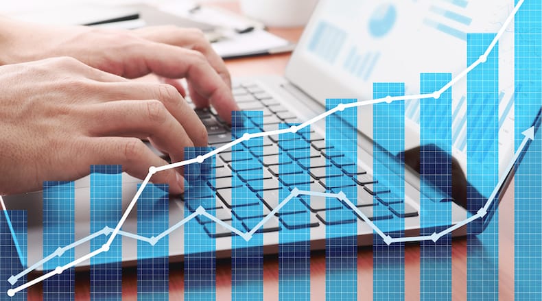 Person typing on a laptop keyboard with overlaid blue bar and line financial graphs indicating growth.