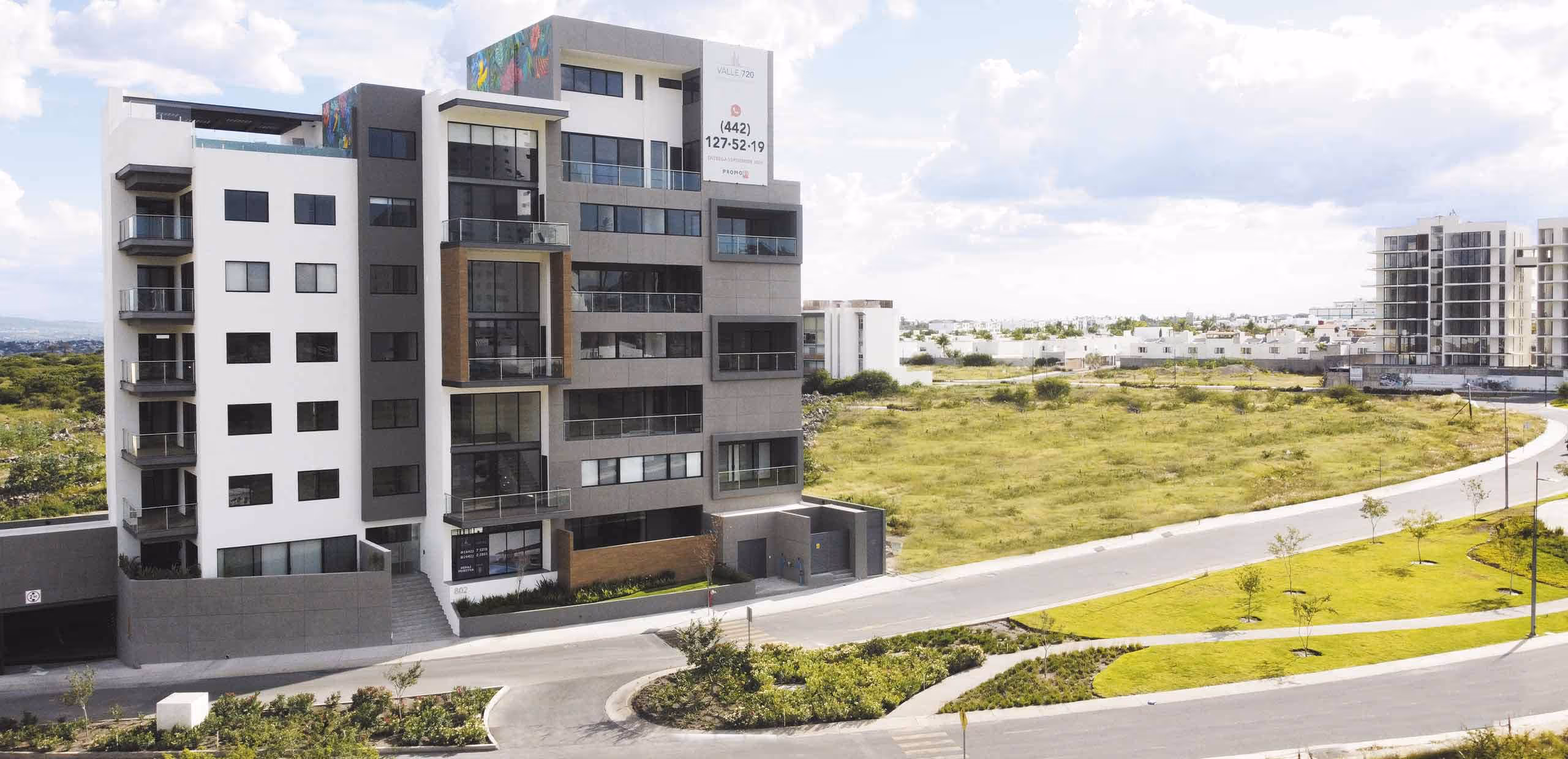 Edificio de departamentos modernos de varios pisos con balcones, rodeado de áreas verdes y un camino curvo.