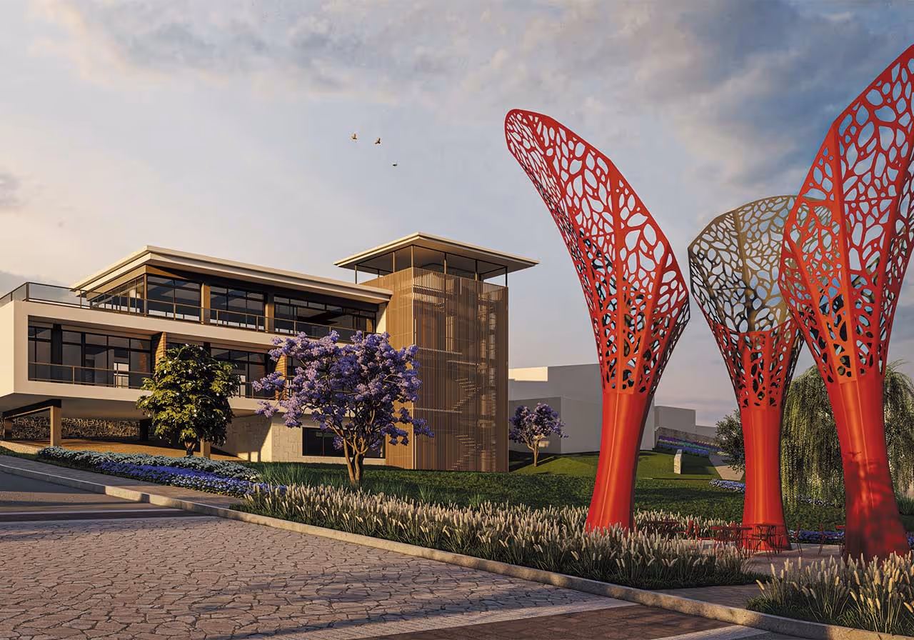 Estructura arquitectónica moderna con tres esculturas rojas grandes de forma orgánica y árboles con flores moradas en un jardín al frente.