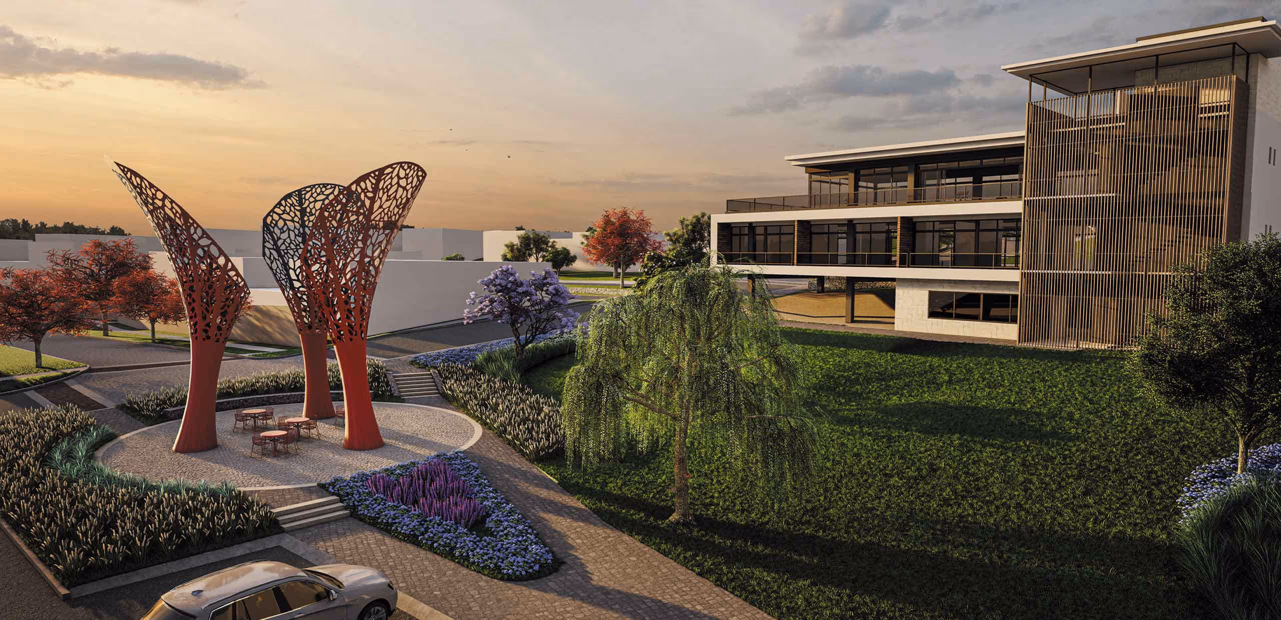Área de jardín con esculturas rojas modernas, mesas con sillas, árboles y edificio moderno al fondo al atardecer.