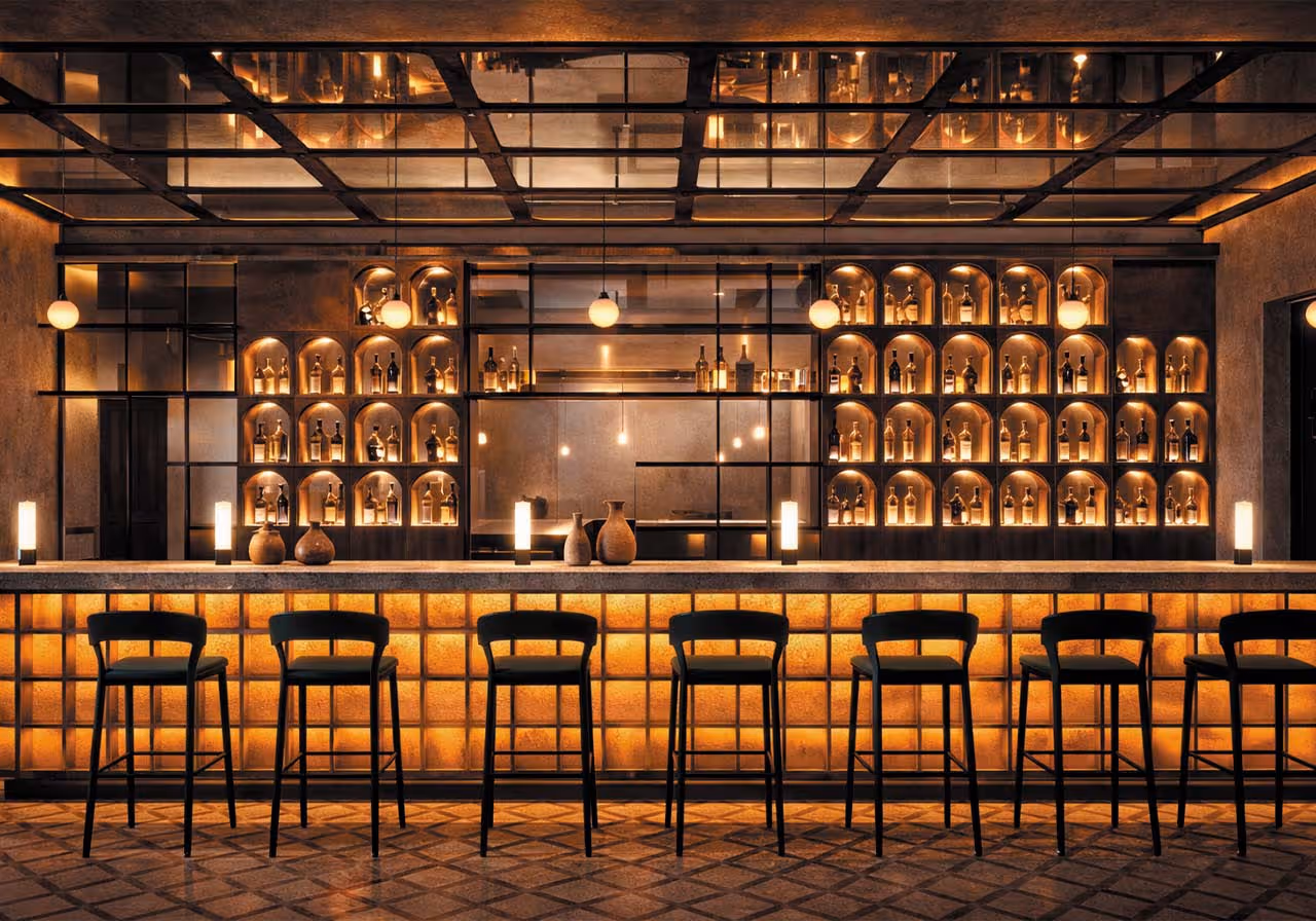 Bar moderno con iluminación cálida, estantes con botellas encajonadas y seis bancos altos alineados frente a la barra.