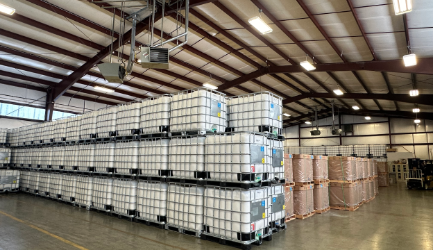 Farm machinery harvesting and loading crops in large rows next to green orchard trees under a clear sky.