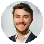 Smiling young man with light brown hair, beard, wearing a white shirt and dark blazer, against a gray background.