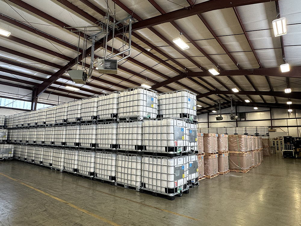 Large warehouse interior with stacked white industrial containers and wrapped palletized goods.