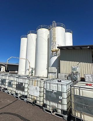White industrial storage tanks and large white containers arranged outside under a clear blue sky.