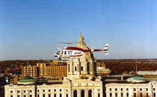 Helicopter flying near a classical building with a dome under a clear blue sky.
